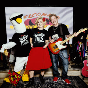 A man and a woman posing with Country This T-shirts adult (unisex) and a mascot.