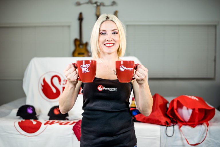 A blonde woman holding up two red coffee mugs.