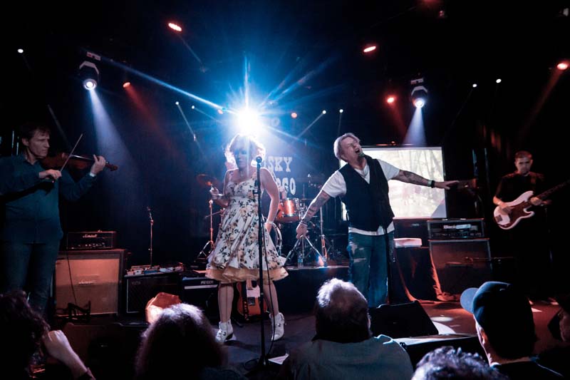 A group of people singing on stage in front of a bright light.